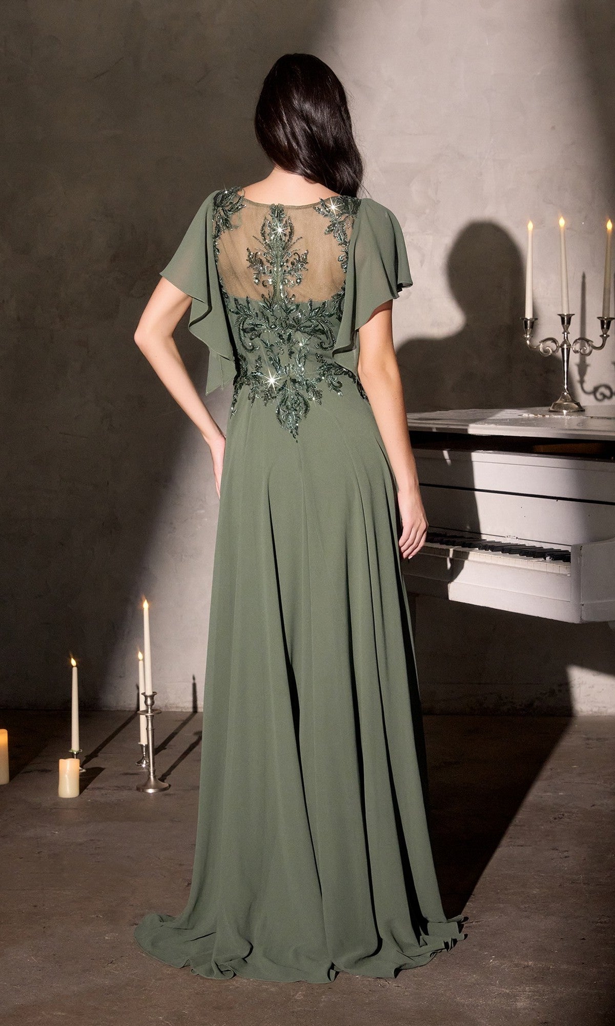 A woman wearing the Ladivine CL09 Long Formal Dress with a sheer embroidered back stands beside a white piano in a dim, candle-lit room, facing away.